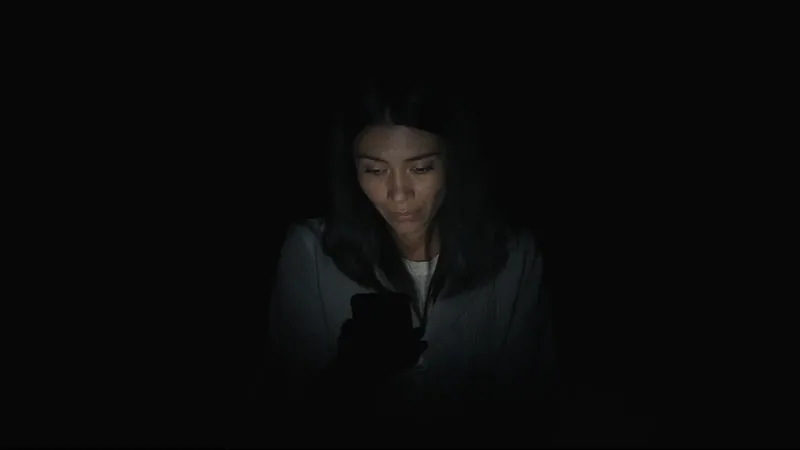 A woman's face lit only by her phone screen in a completely dark room