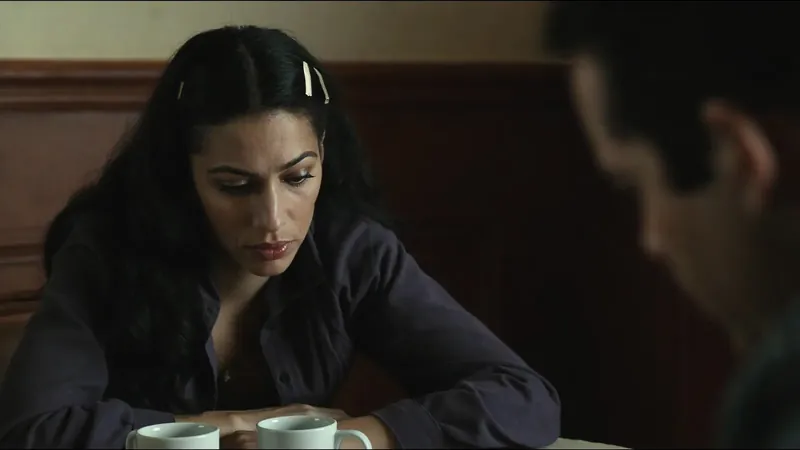 A woman looking down at a table with two coffee cups while a man sits out of focus in the foreground