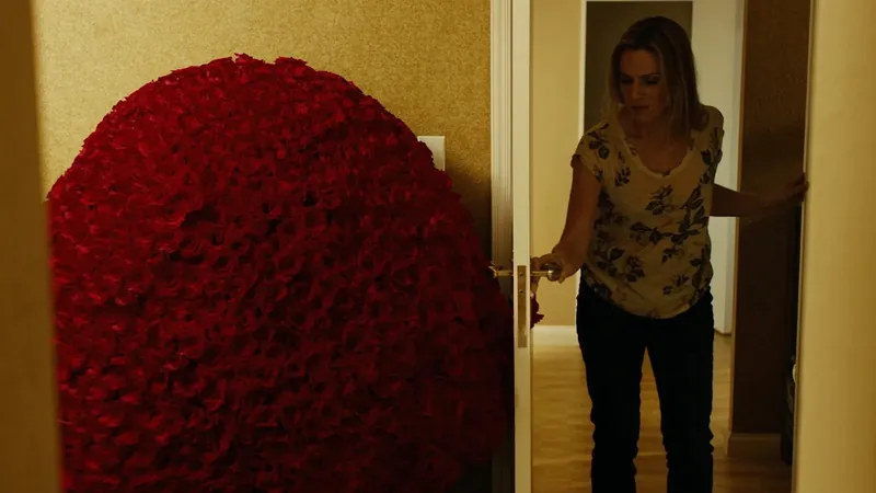 A woman opening a door to find an enormous heart made of red roses filling the hallway