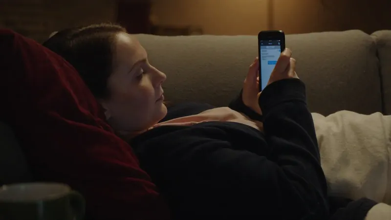 A woman lying on a sofa in lamplight, reading a message on her phone