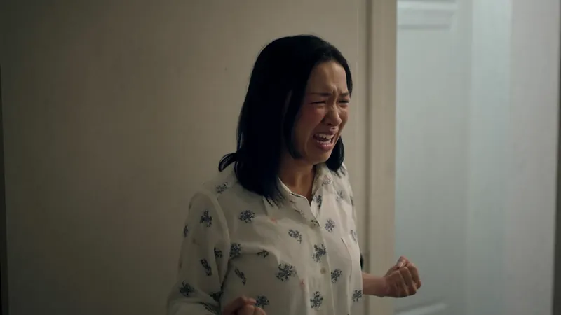 A woman in pajamas standing in a doorway, her face crumpled in tears and one fist clenched