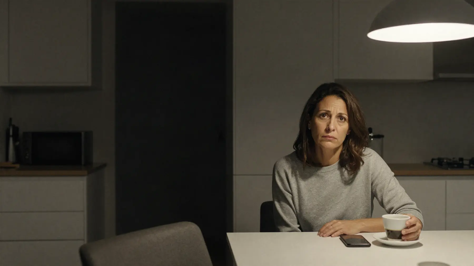 A woman at the kitchen table at night with a cup and her phone face down