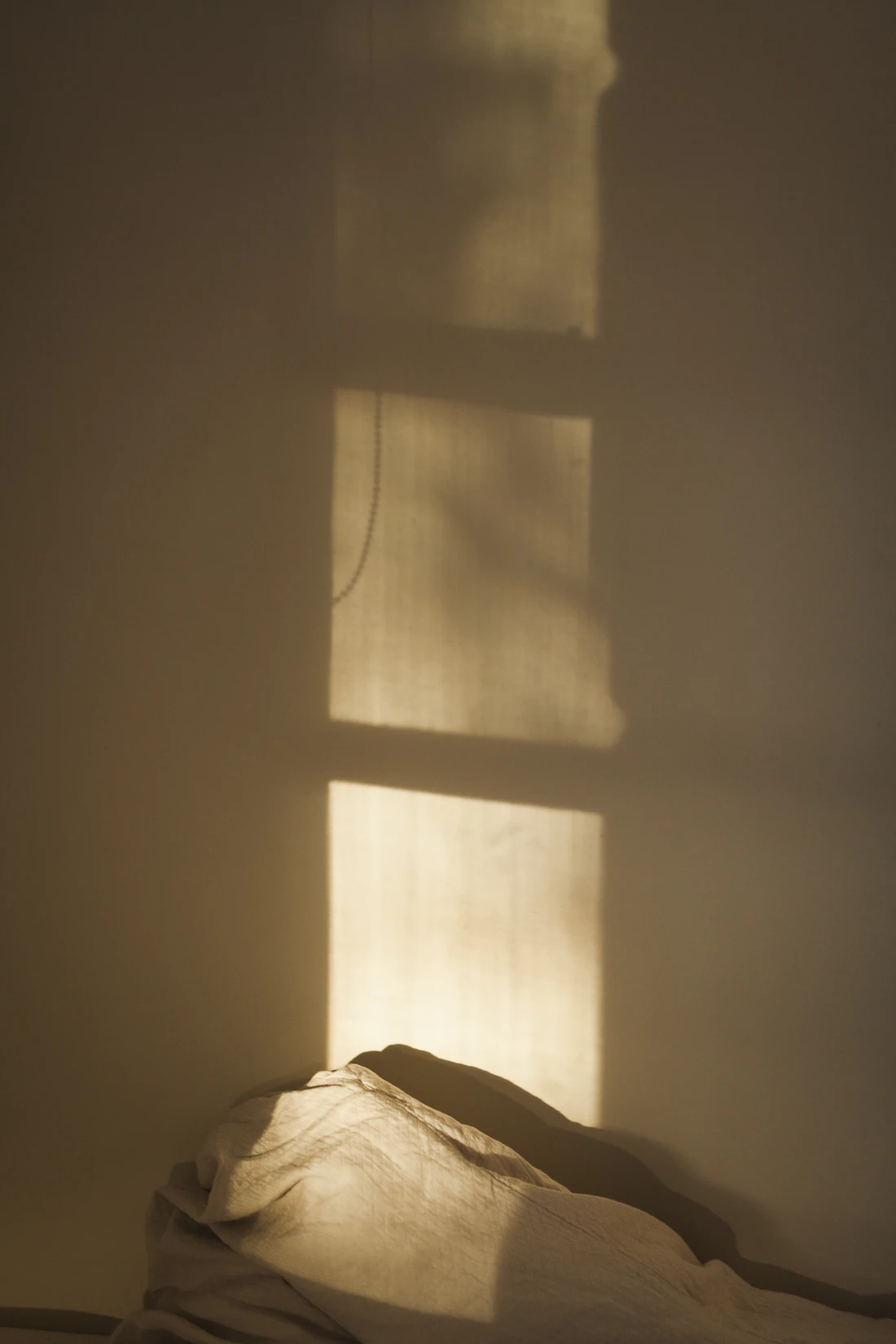 Morning light falling across a wall and the corner of an unmade bed